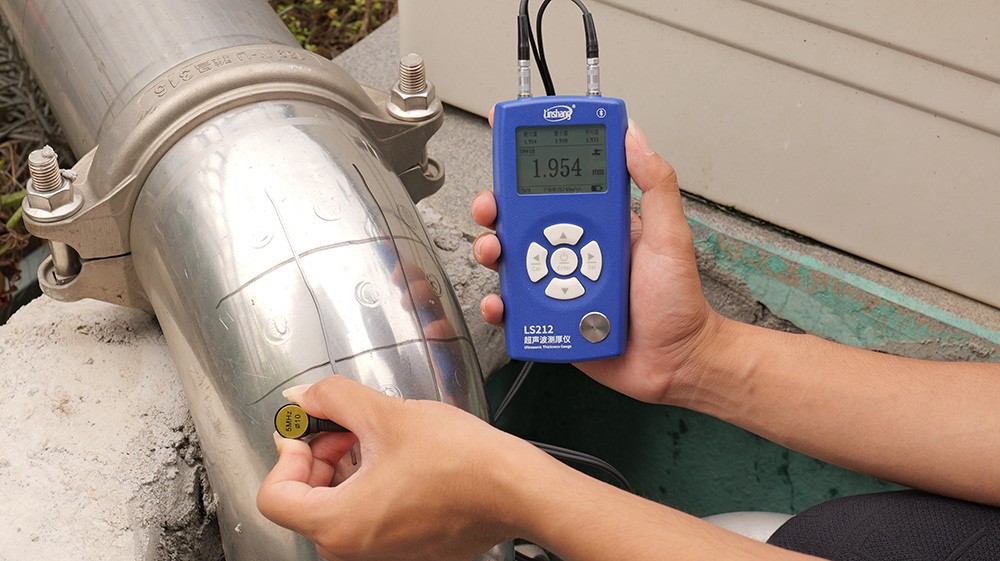 林上LS212超声波测厚仪(蓝色机身)测量金属管道,显示屏4.685mm,墙面绘有测点布置示意(沿管道周向标记红点测点)