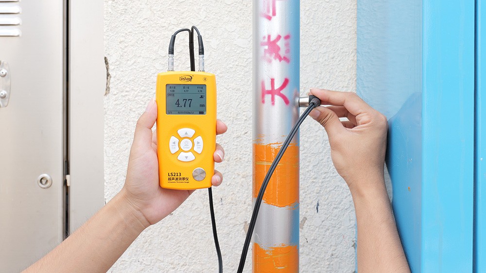 林上LS213超声波测厚仪(黄色机身)实测户外蓝色立管,显示壁厚4.77mm,管身周围已用记号笔标记截面四点法测点位置(东/南/西/北侧),用于长期腐蚀趋势监测